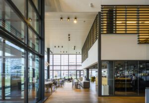 Moderne, open kantoorlobby aan de Thomas R. Malthusstraat met hoge plafonds, veel glas en een koffiebar.